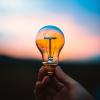 Hand holding a light bulb in front of a sunrise