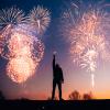 Person holding sparkler with New Year's fireworks in the background